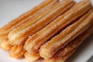 Baked churros dusted with cinnamon sugar on a plate for a healthier alternative to traditional deep-fried churros.

