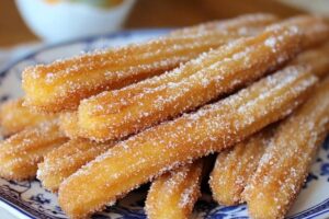 Baked churros dusted with cinnamon sugar on a plate for a healthier alternative to traditional deep-fried churros.

