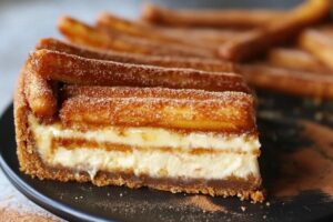 A slice of churro cheesecake with cinnamon sugar topping, layered with cream cheese filling and golden crescent roll crust.

