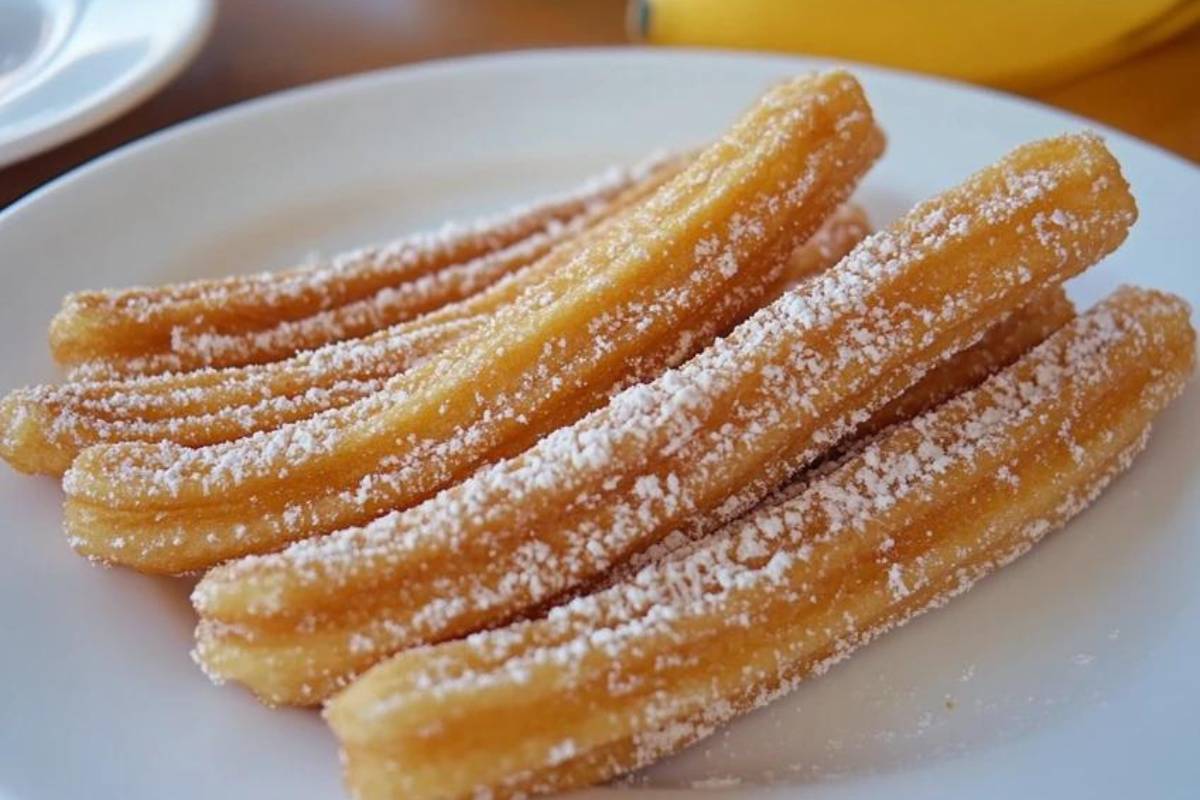 A plate of filled churros topped with cinnamon sugar, chocolate drizzle, and caramel, garnished with crushed nuts and whipped cream.