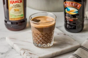 Espresso Martini cocktail with Kahlúa and Baileys bottles on a wooden table.