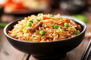 Restaurant-style Chinese fried rice in a wok, featuring fluffy rice, colorful vegetables, and savory seasonings like soy sauce and sesame oil. 