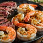 Sizzling garlic glazed steak and shrimp plated with fresh herbs and a garlic glaze drizzle