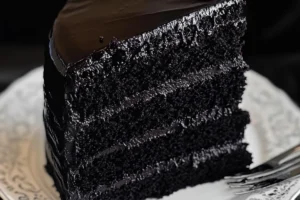 A slice of moist Black Velvet Cake with cream cheese frosting and edible gold leaf garnish.

