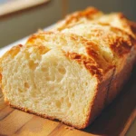 Lemon Cream Cheese Bread 7 iymarecipes Freshly baked lemon cream cheese bread with a golden crust and creamy swirls, sliced on a wooden board.