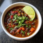 Close-up of a bowl of zesty black bean soup garnished with cilantro and a lime wedge.