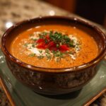 Close-up of a bowl of Easy Stuffed Pepper Soup, garnished with red peppers and herbs.