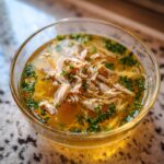 Close-up of a clear glass bowl filled with Fish Broth Cat Recipe, shredded fish, and fresh herbs.