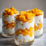 Three glasses of Mango Coconut Pudding Parfait layered with fresh mango and coconut cream.