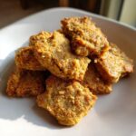 Close-up of a pile of golden-brown Tuna & Oat Cat Crunchies on a white plate.