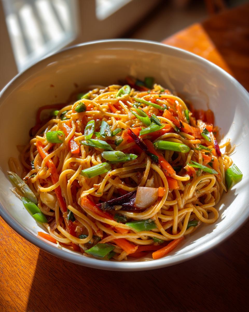 Close-up of Asian pasta salad with noodles, carrots, and green onions in a white bowl.