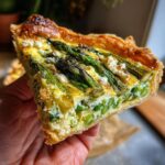 A slice of asparagus tart, perfect for Spring Baking Recipes, held in a hand.