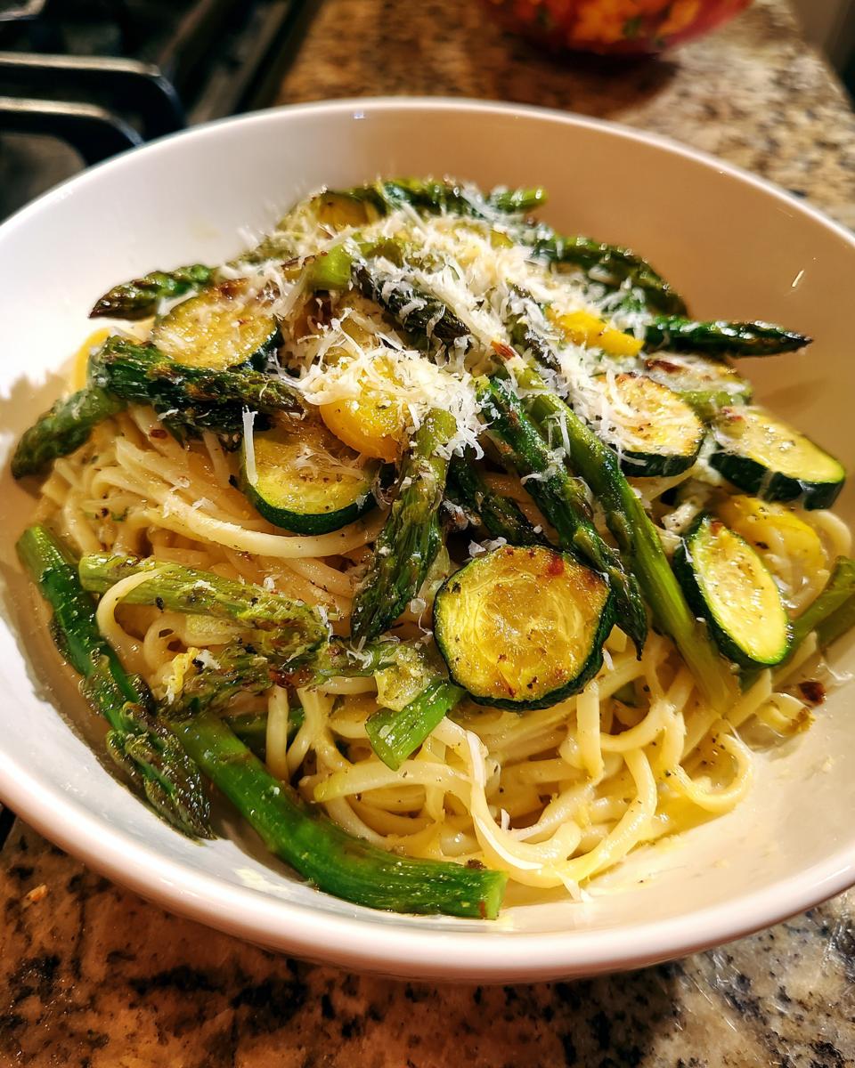 Close-up of a bowl of asparagus and zucchini pasta salad, topped with cheese.