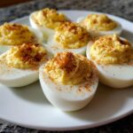 Close-up of classic deviled eggs on a white plate, topped with paprika.