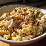 Close-up of creamy pasta salad and chicken in a white bowl, garnished with herbs.