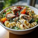 Close-up of a pasta salad and chicken bowl with tomatoes, lettuce, and creamy dressing.