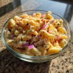 Close-up of a bowl filled with pasta salad and chicken, with red onion and spices.
