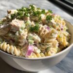 Close-up of a creamy pasta salad and chicken in a white bowl, garnished with parsley. The pasta salad and chicken is a delicious and easy meal.