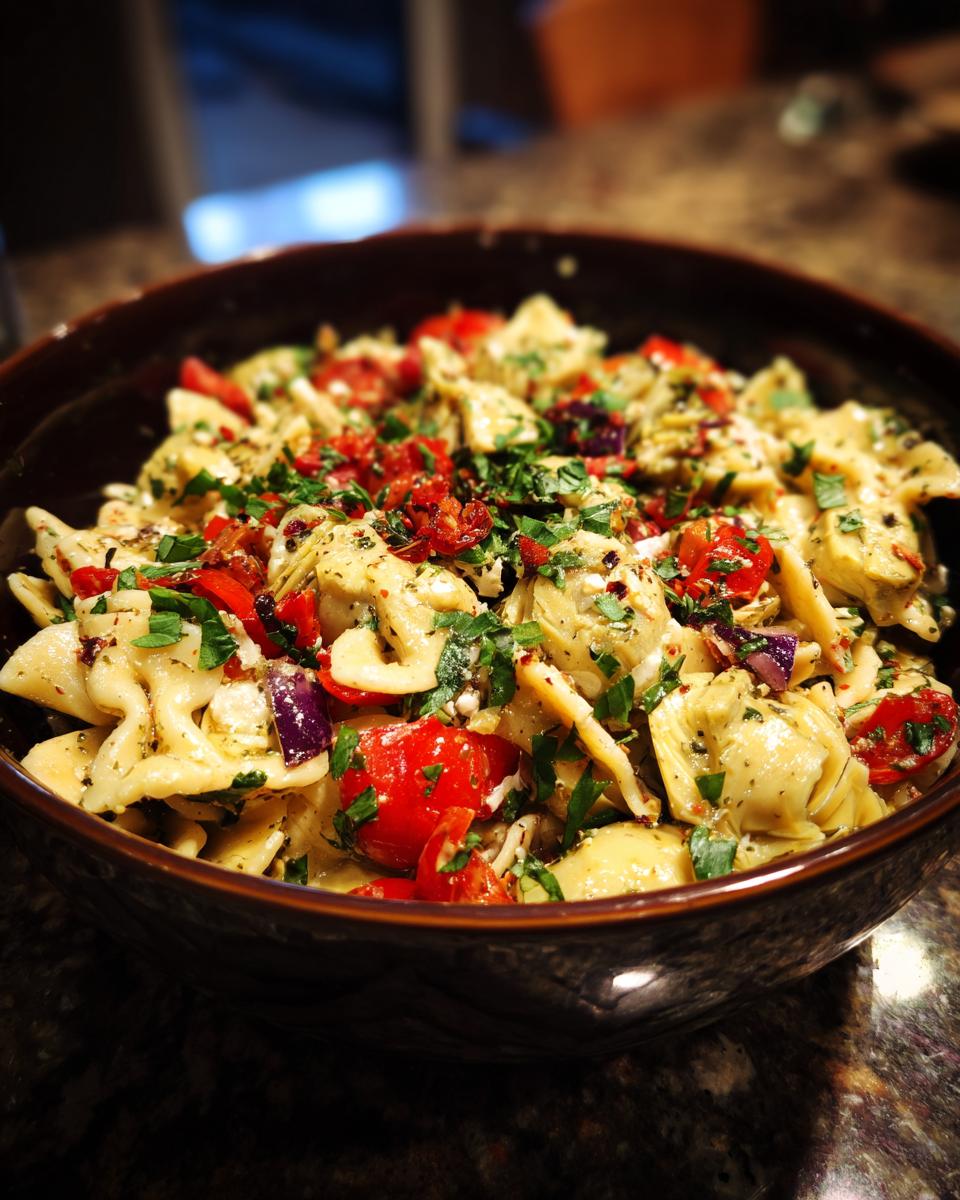 Close-up of a bowl of pasta salad artichoke with tomatoes, herbs, and red onion.