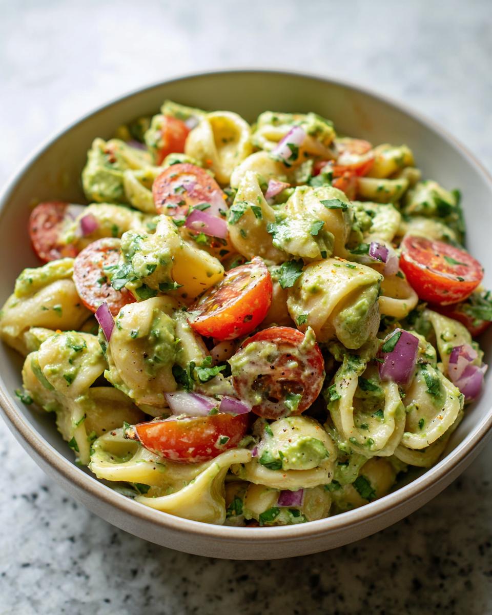 Close-up of pasta salad avocado with tomatoes, red onion, and herbs in a bowl.
