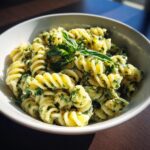 Close-up of pasta salad basil with fresh basil leaves in a white bowl.