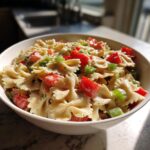 Bowl of delicious pasta salad bowtie with tomatoes, green onions, and creamy dressing. The pasta salad bowtie is ready to eat.