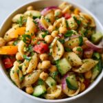 Close-up of a pasta salad chickpeas in a white bowl with vegetables and herbs.