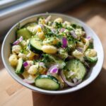 Close-up of a bowl of pasta salad cucumber with fresh dill and red onion.