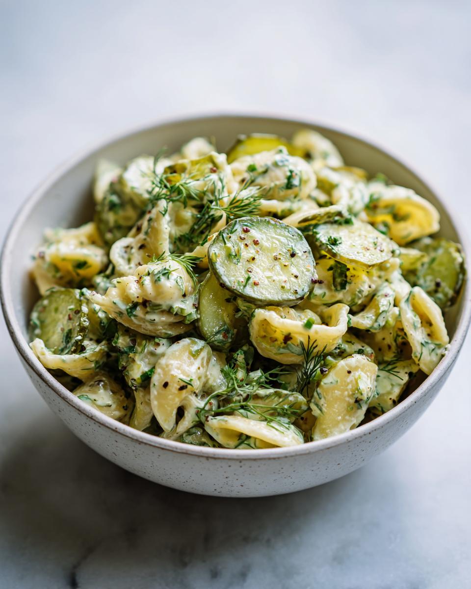 Close-up of creamy pasta salad dill pickle in a white bowl, garnished with fresh dill.