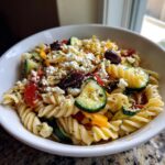 Close-up of a bowl filled with Greek pasta salad, featuring pasta, vegetables, feta, and olives. This is a pasta salad greek.