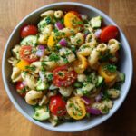 Close-up of a bowl of pasta salad with tomatoes, cucumber, and herbs. This is a pasta salad healthy recipe.