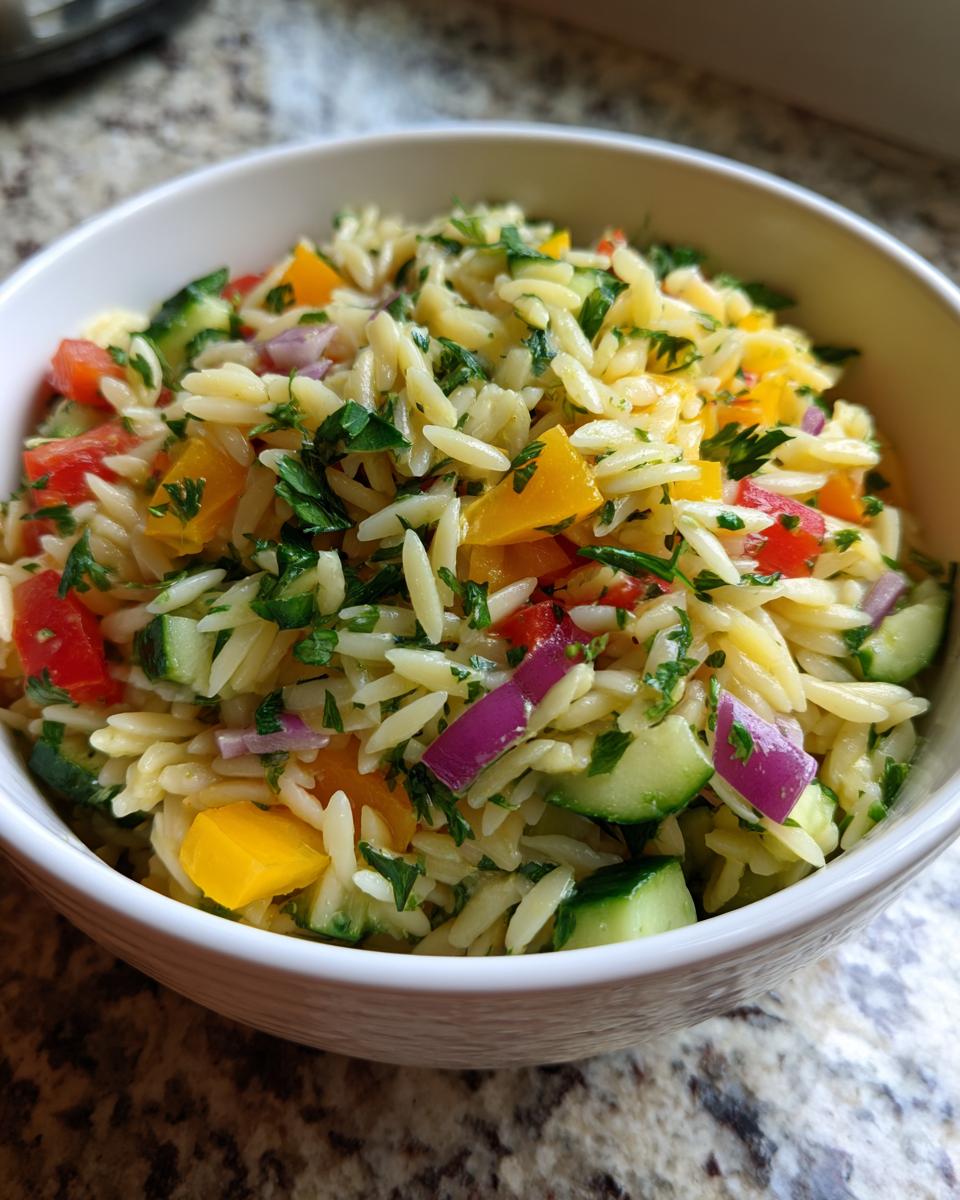 Close-up of a bowl of pasta salad orzo with colorful vegetables and herbs.