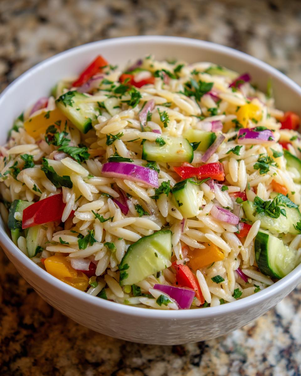 Close-up of a vibrant pasta salad orzo with cucumbers, peppers, and red onion in a white bowl.