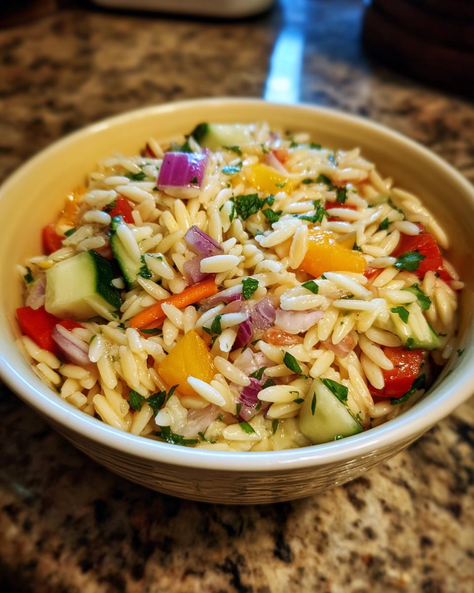 Close-up of a bowl of pasta salad orzo with colorful vegetables and herbs.
