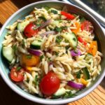 A vibrant bowl of pasta salad orzo with tomatoes, cucumbers, and red onion.