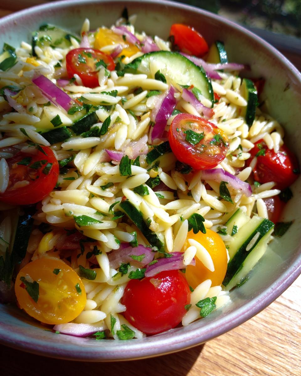 Close-up of pasta salad orzo with cherry tomatoes, cucumbers, red onion, and herbs.
