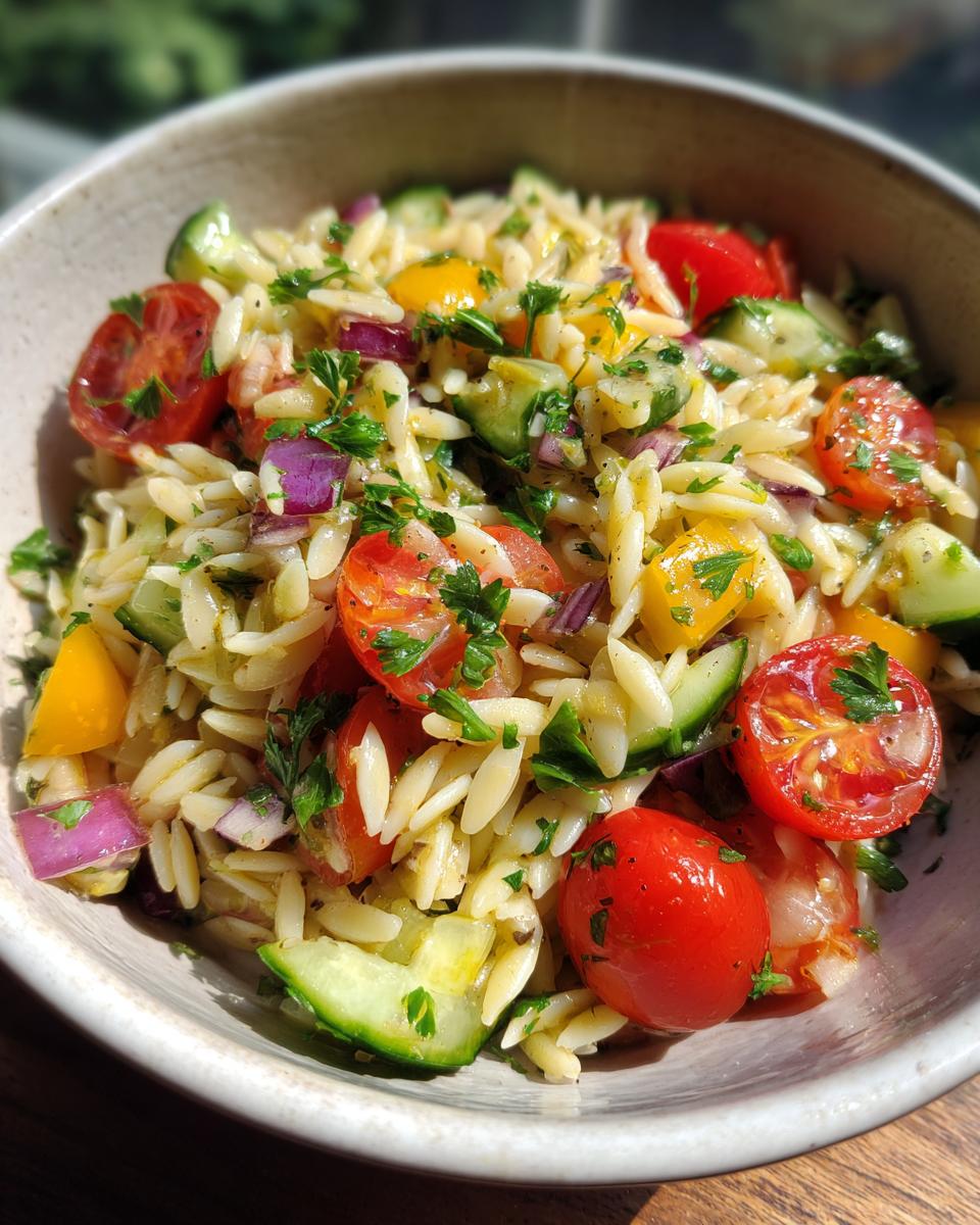 Close-up of a bowl of pasta salad orzo with cherry tomatoes, cucumber, and herbs.