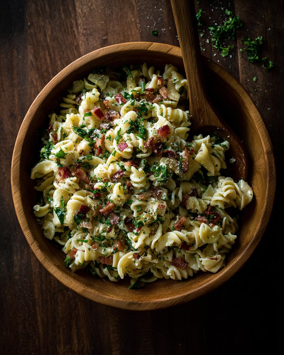 Overhead shot of creamy pasta salad spring with bacon and fresh herbs in a wooden bowl.