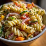 Close-up of a bowl of pasta salad with spiral pasta, vegetables, and herbs. How do you make pasta salad?